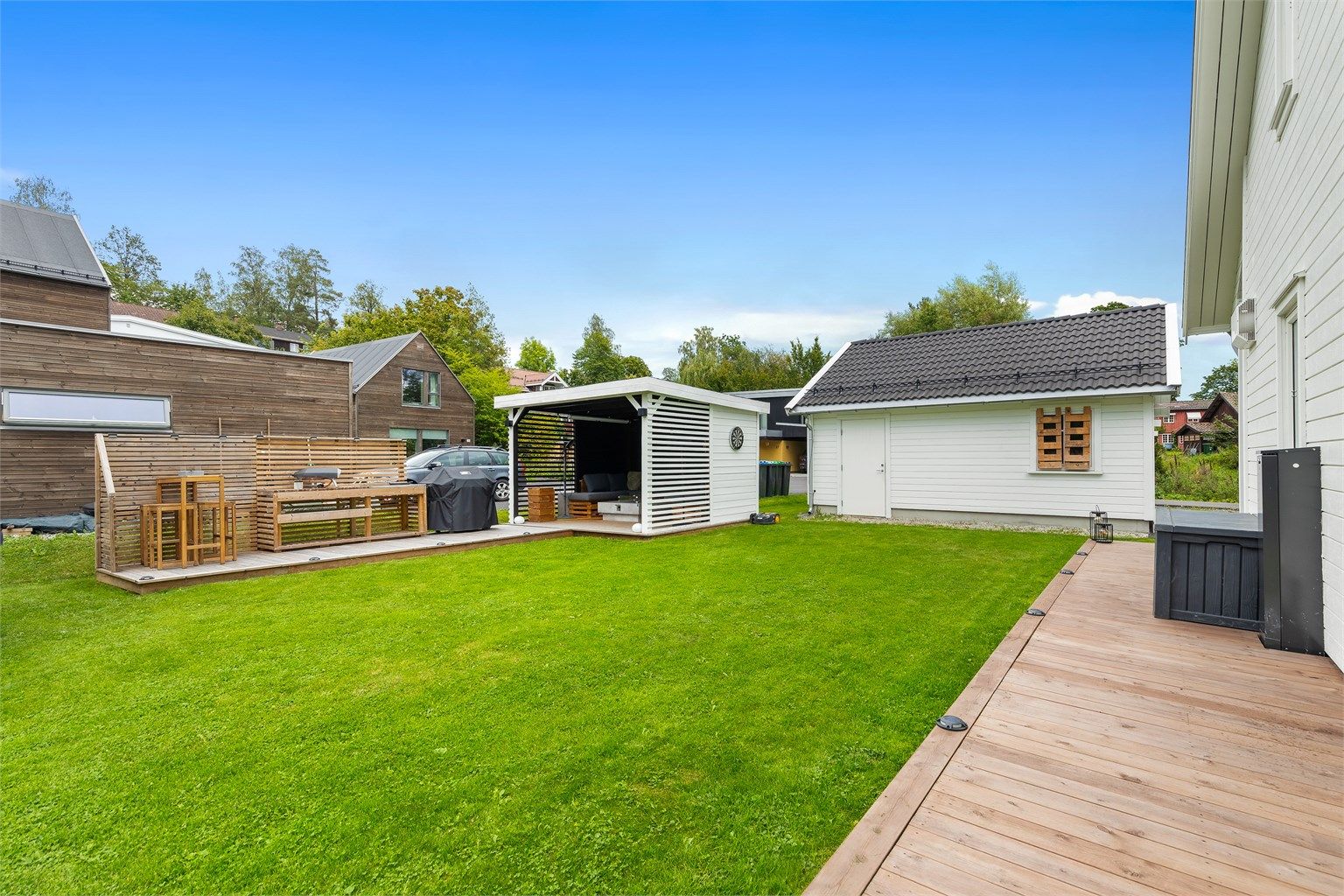 Hage med plen, platting og pergola.