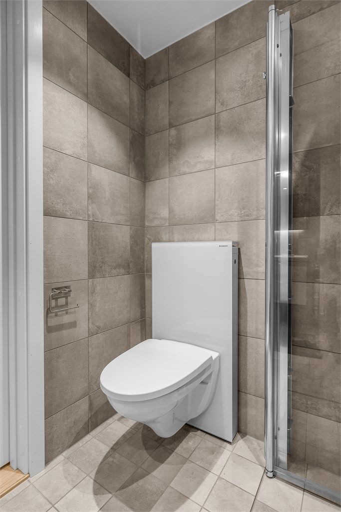 Badet er utstyrt med vegghengt toalett og dusjhjørne med innfellbare glassdører.