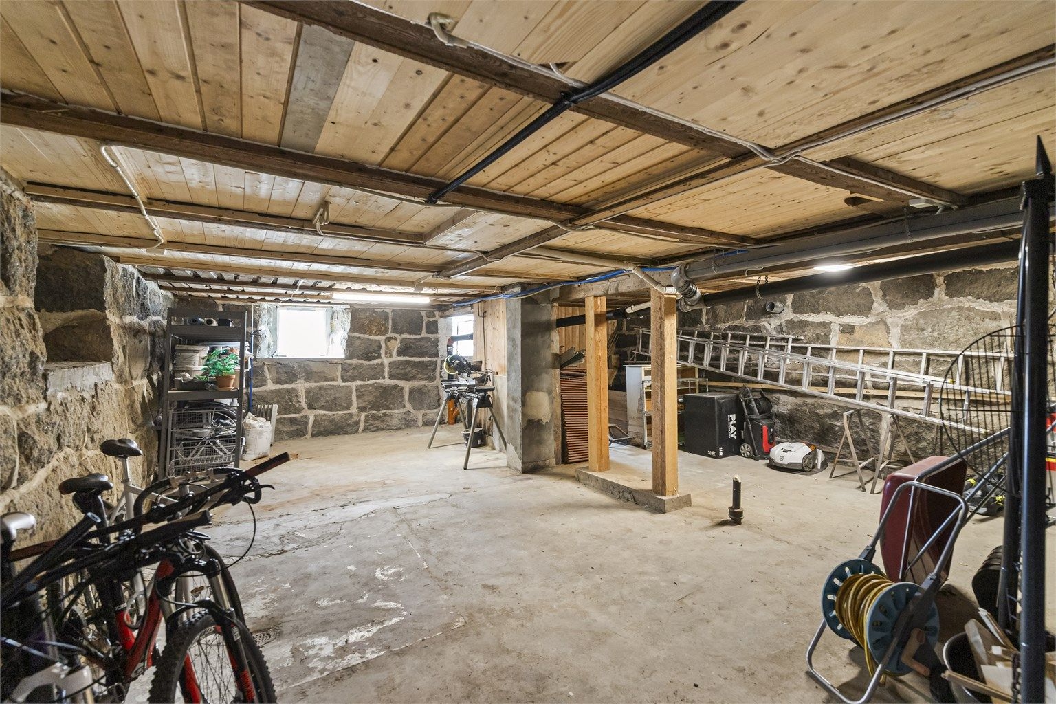 Kjelleren har vegger i naturstein og gulv av støpt betong og jord, og gir rikelig med lagringsplass.