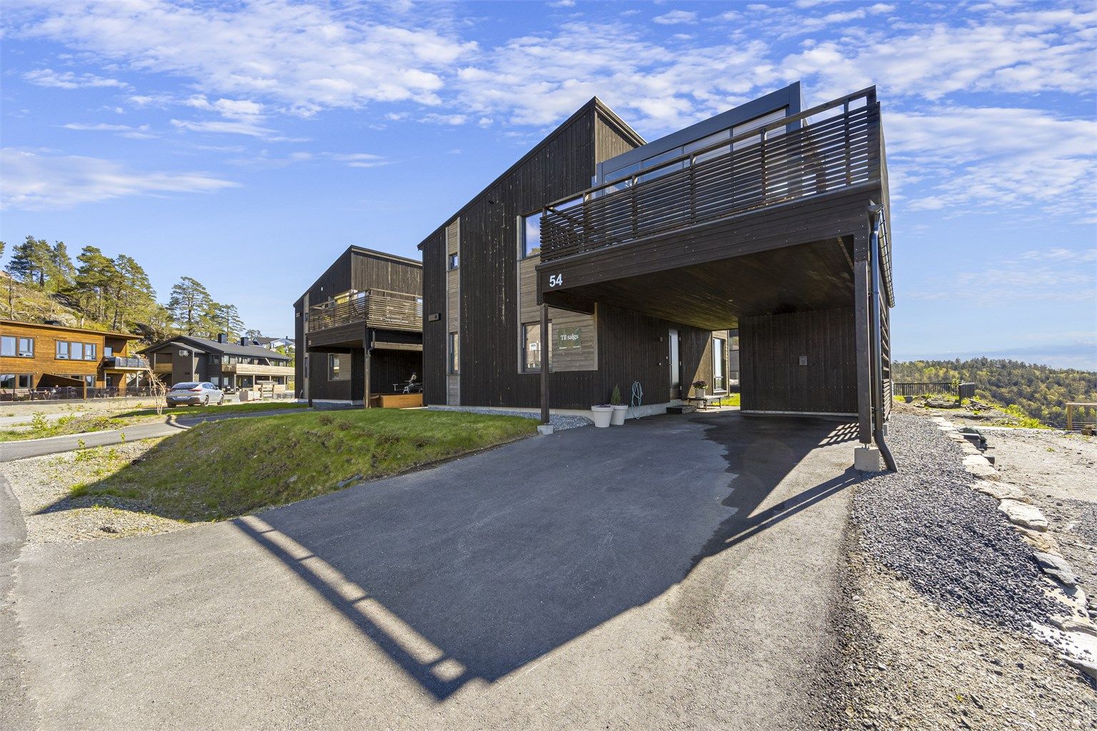 Det er asfaltert innkjørsel og carport med bod i enden. Elbillader er installert på vegg til boden.