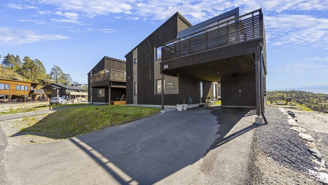 Det er asfaltert innkjørsel og carport med bod i enden. Elbillader er installert på vegg til boden.