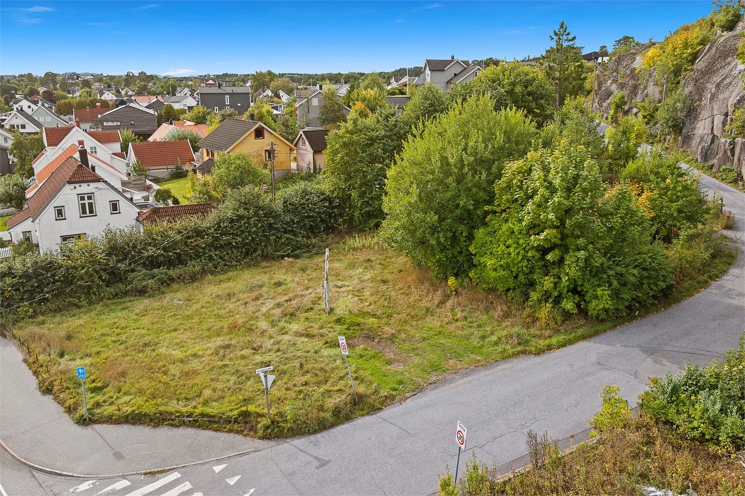 Tomten har veiadkomst fra Lystadsvingen og grenser til grønne omgivelser og fjellknaus i bakkant.
Foto: [Fotograf eller fotofirma]