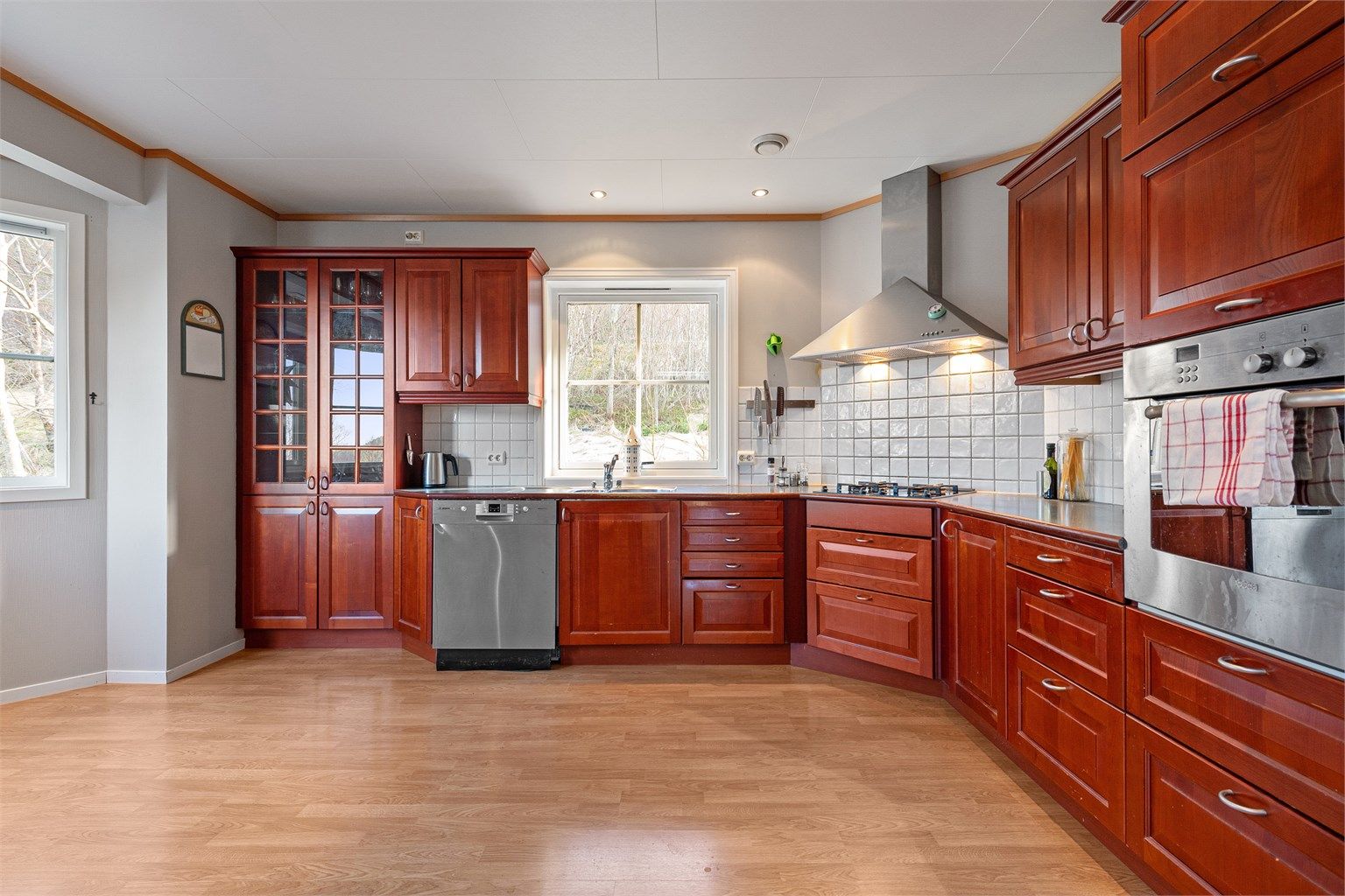 Kjøkkeninnredning fra HTH med profilert fronter i kirsebærfiner. Det er ventilatorhette over integrert koketopp med gassbluss, integrert stekeovn, opplegg for vaskemaskin. 