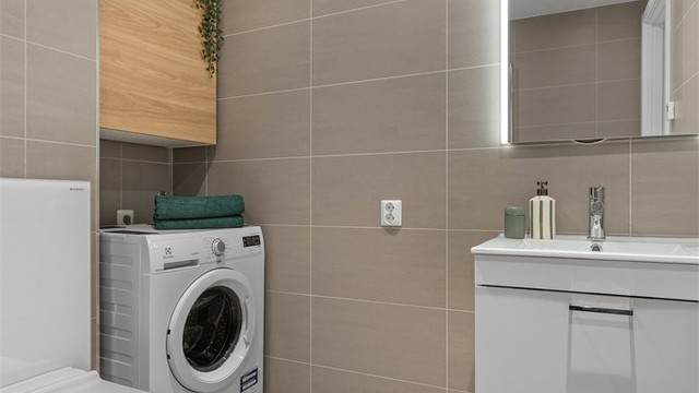 Moderne standard med vegghengt servantskap med speil ovenfor, vegghengt toalett og dusj med innfellbare glassdører.
