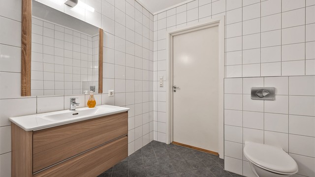 Flislagt bad med servantskap, dusjhjørne og toalett