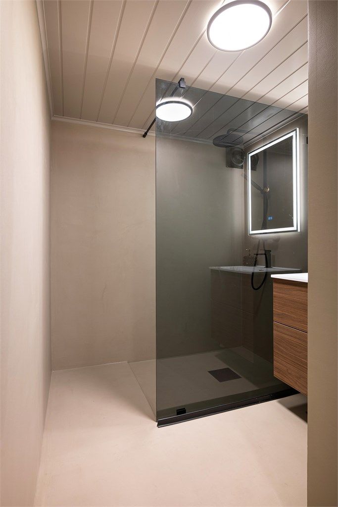 Badet er stilfullt pusset opp i 2026 med microsement på gulv og vegger, nytt dusjhjørne og nye møbler. I gulvet er det varmekabler av eldre årgang.