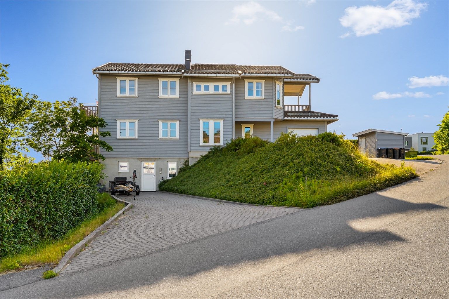 Eiendommen ligger på en skrånende tomt med opparbeidet plen og beplantning.