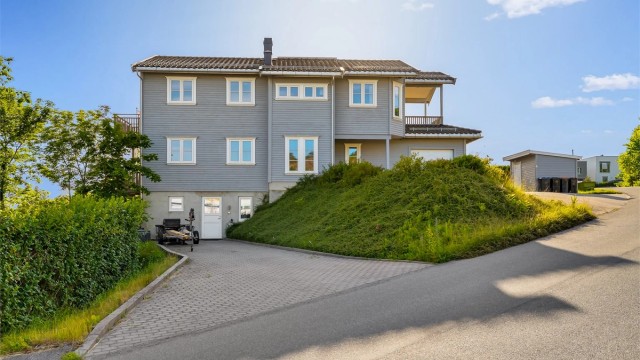 Eiendommen ligger på en skrånende tomt med opparbeidet plen og beplantning.