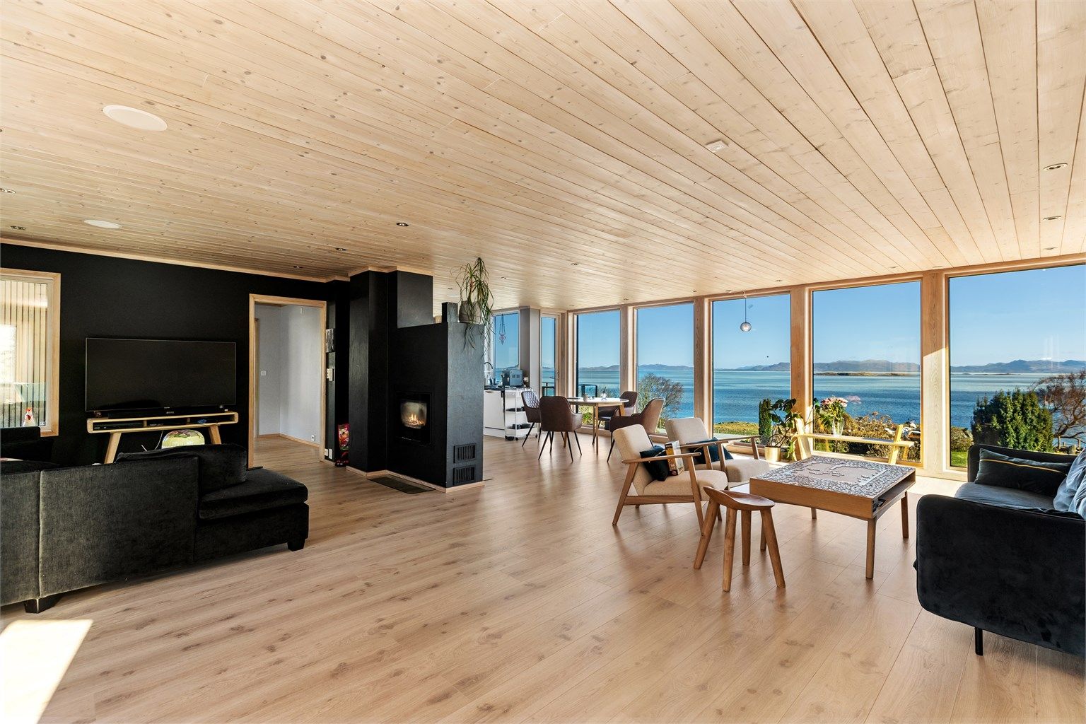 Stuen og kjøkkenet utgjør et stort allrom med panelbord i himling og store vindusflater som rammer inn utsikten mot sjøen.