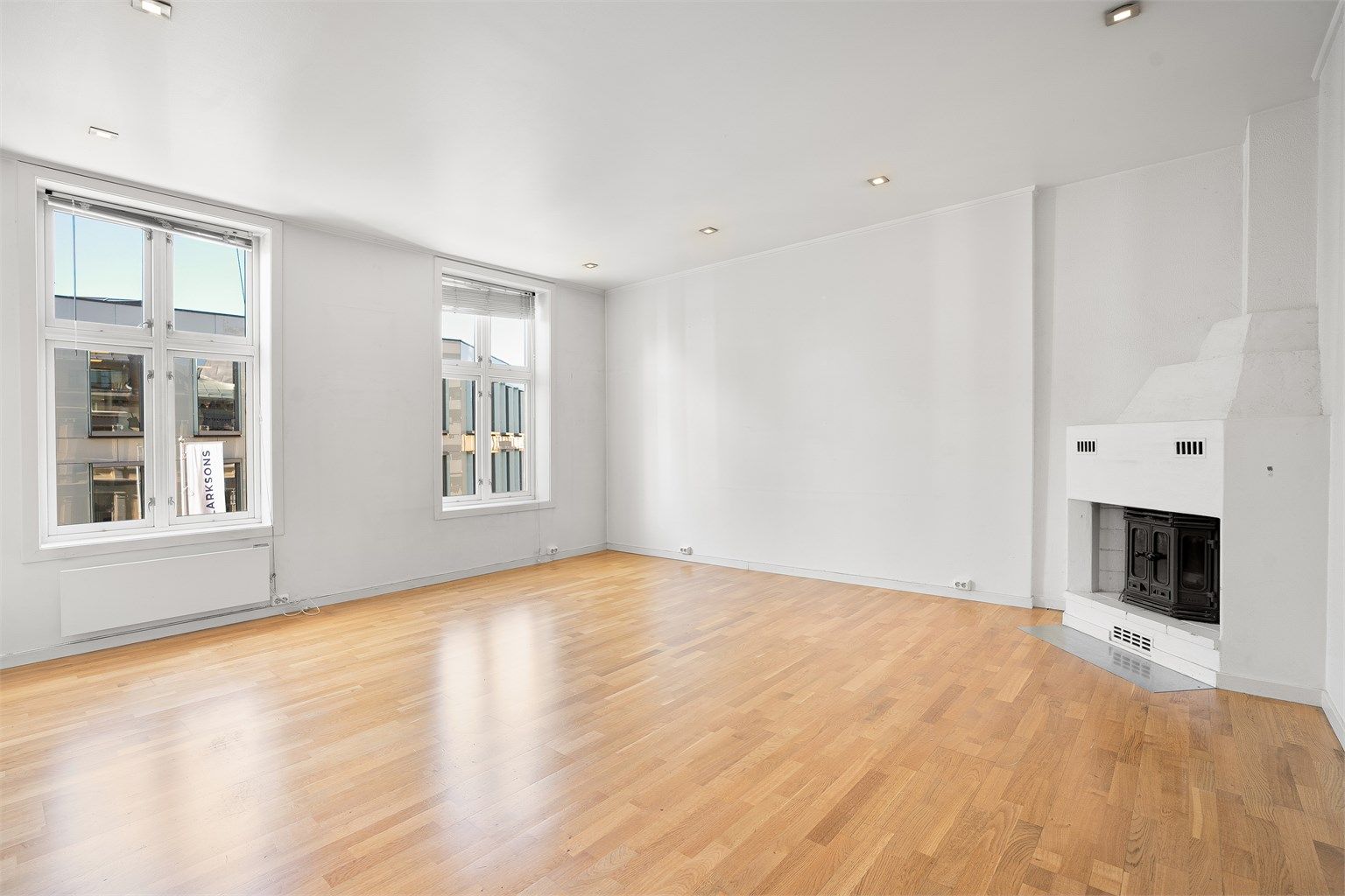 Stue med store vindusflater og peis i hjørnet som gir leiligheten et koselig særpreg.