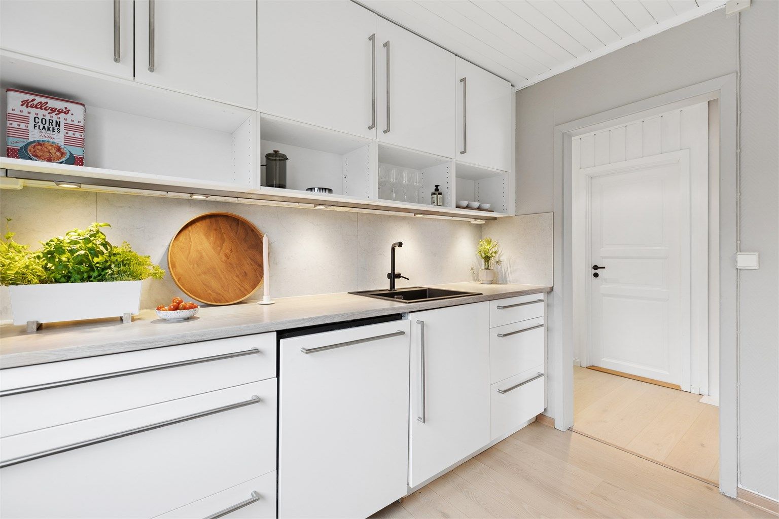 Kjøkkeninnredning med glatte fronter, laminat benkeplate og belysning under overskapene.