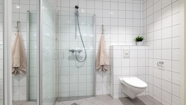 Dusjhjørne med vegghengt armatur og vegghengt toalett med skjult sisterne.