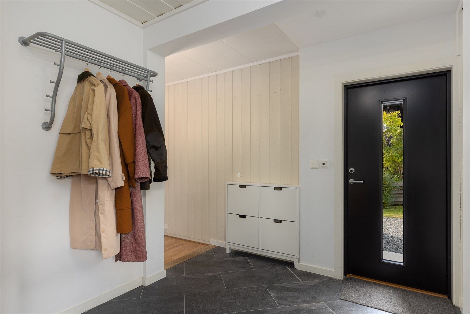 Entré i 1. etasje med mørke fliser, gulvvarme og inngangsdør i dels glass som slipper inn naturlig lys