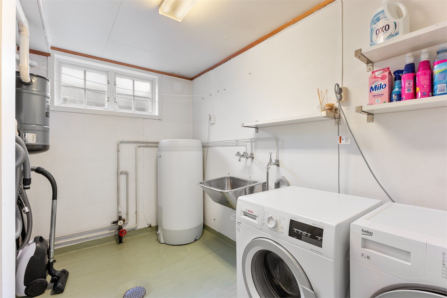 Praktisk vaskerom med varmekabler, opplegg for vaskemaskin og plassering av sentralstøvsuger.