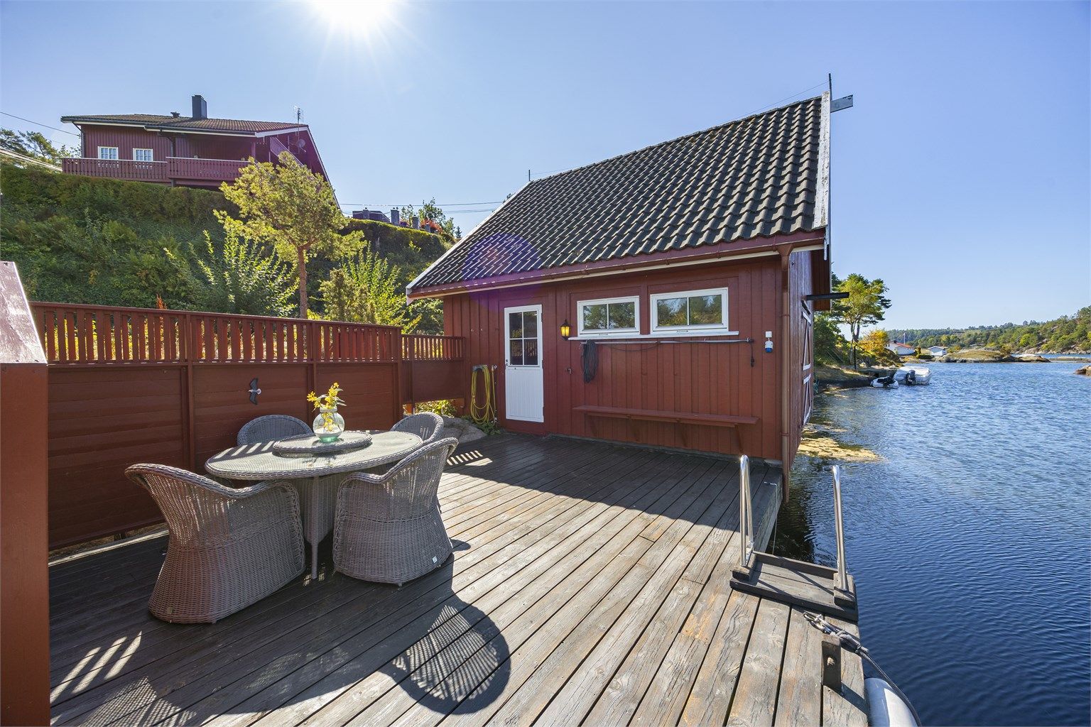 Eget båthus med loft og terrasseplatting ved sjøen.