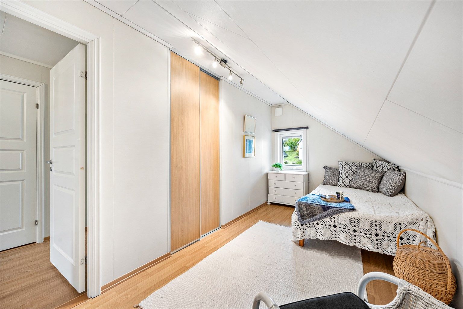 Soverom i loftsetasjen innredet med skyvedørsgarderobe og laminatgulv.