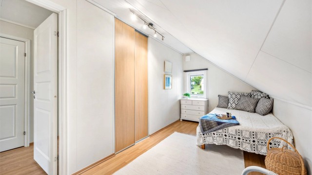 Soverom i loftsetasjen innredet med skyvedørsgarderobe og laminatgulv.