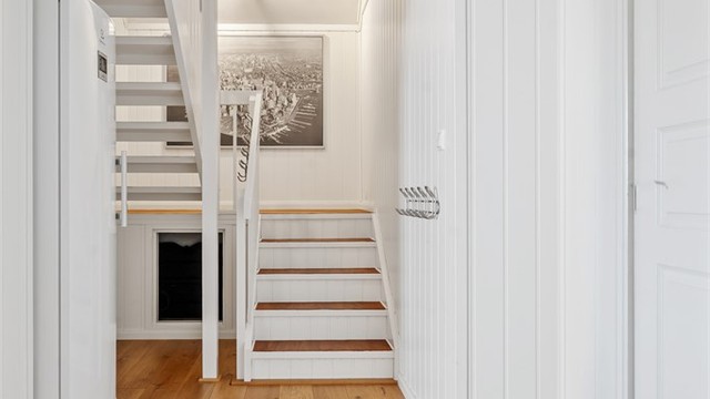 Lys entré med trapp i trekonstruksjon som leder opp til loftsetasjen.