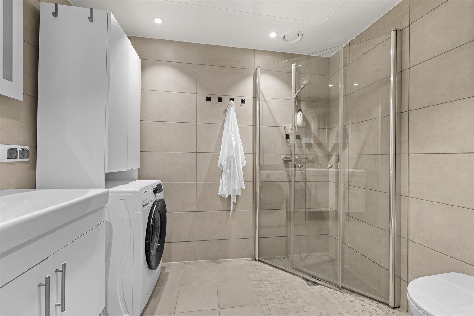 Moderne bad/wc med plasseringsmulighet for vaskemaskin. Lekre innfellbare dusjevegger i herdet glass. Vegghengt wc i hvit porselen. 
