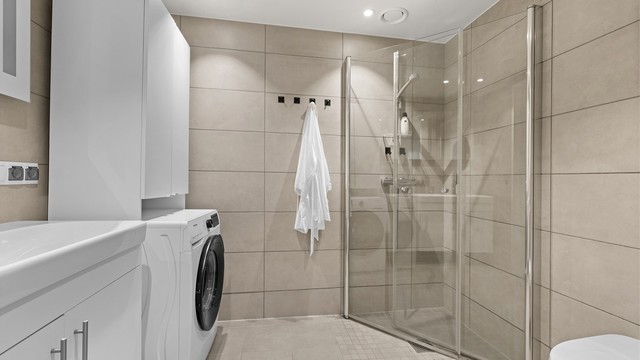 Moderne bad/wc med plasseringsmulighet for vaskemaskin. Lekre innfellbare dusjevegger i herdet glass. Vegghengt wc i hvit porselen.