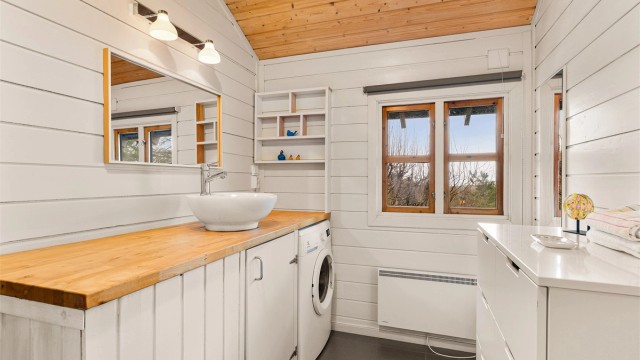 Badet er stilrent og enkelt med vaskemaskin, dusjkabinett og bolleservant plassert på en enkel innredning.