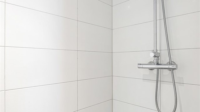 Dusjnisje med dusjdør av glass og veggmontert regnfallsdusj.