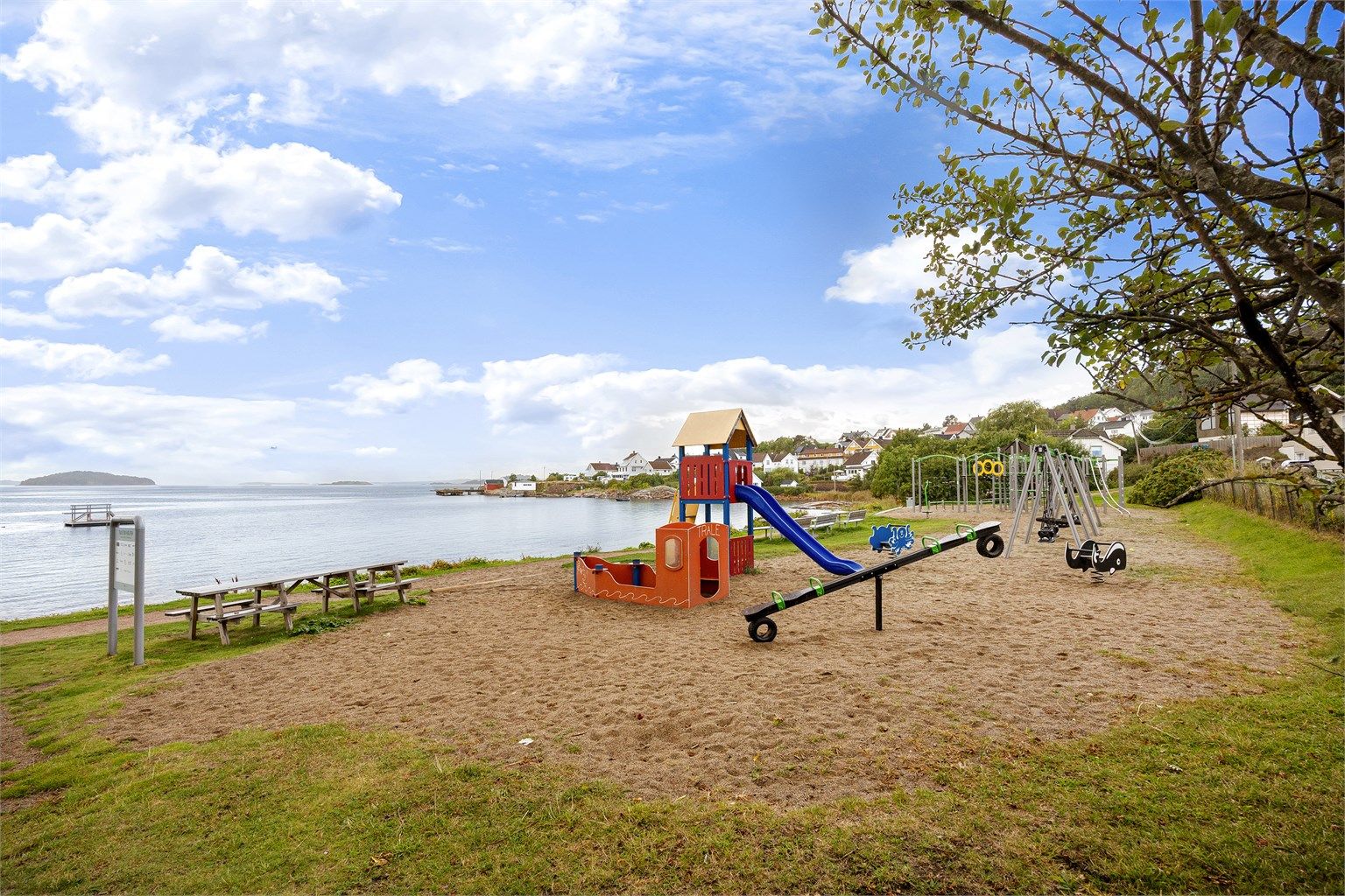 Barnevennlig strand med lekeplass og sittebenker i nærområdet.