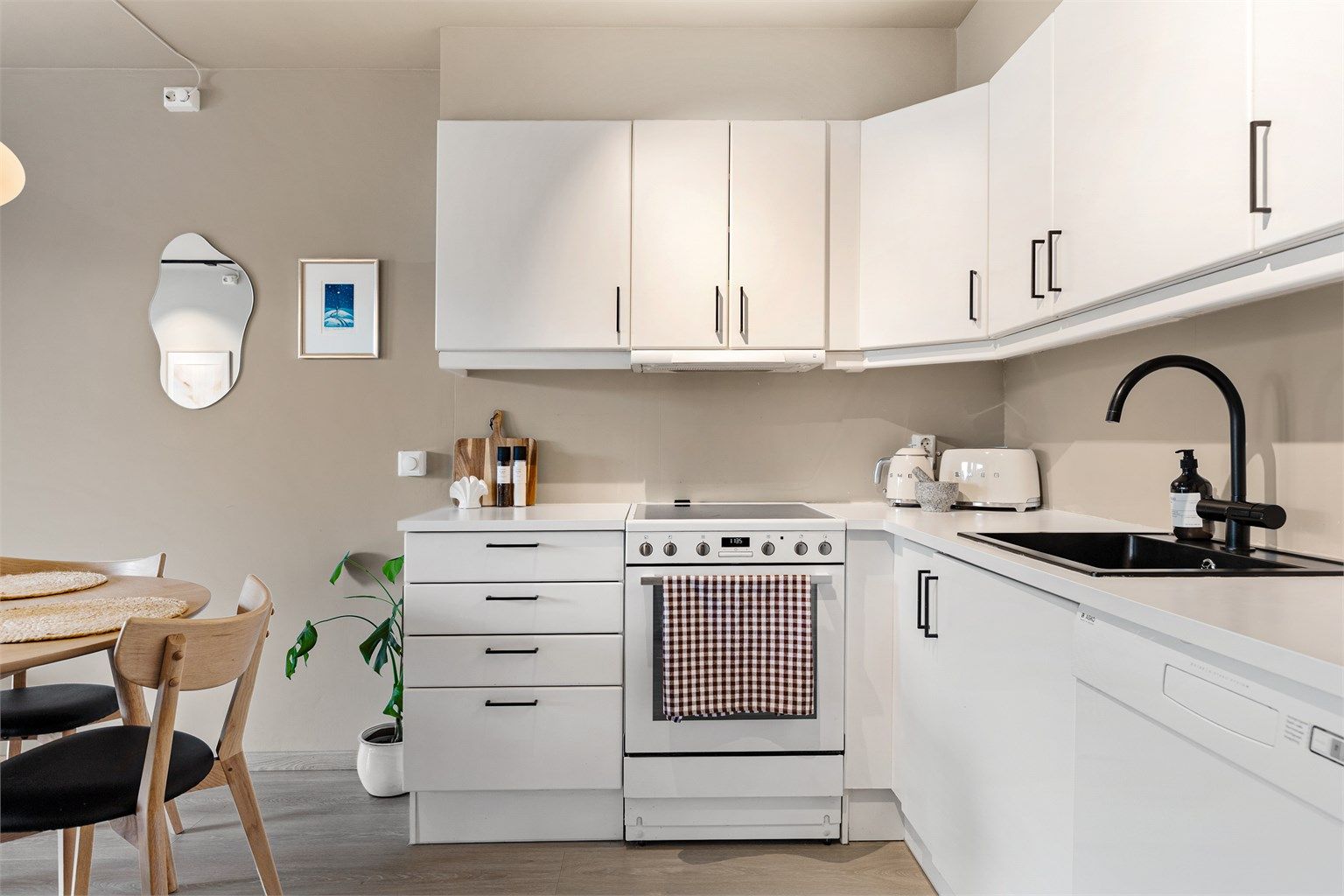 Kjøkkenvask med armatur. Frittstående komfyr, oppvaskmaskin og kjøleskap med fryser. Ventilator integrert i overskap, tilknyttet boligens mekaniske avtrekksventilasjon. Varmtvannsbereder er praktisk plassert under kjøkkenbenken.