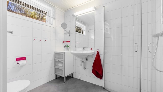 Pent flislagt bad på 4 kvm med servant, speil og lys, toalett og dusjhjørne.