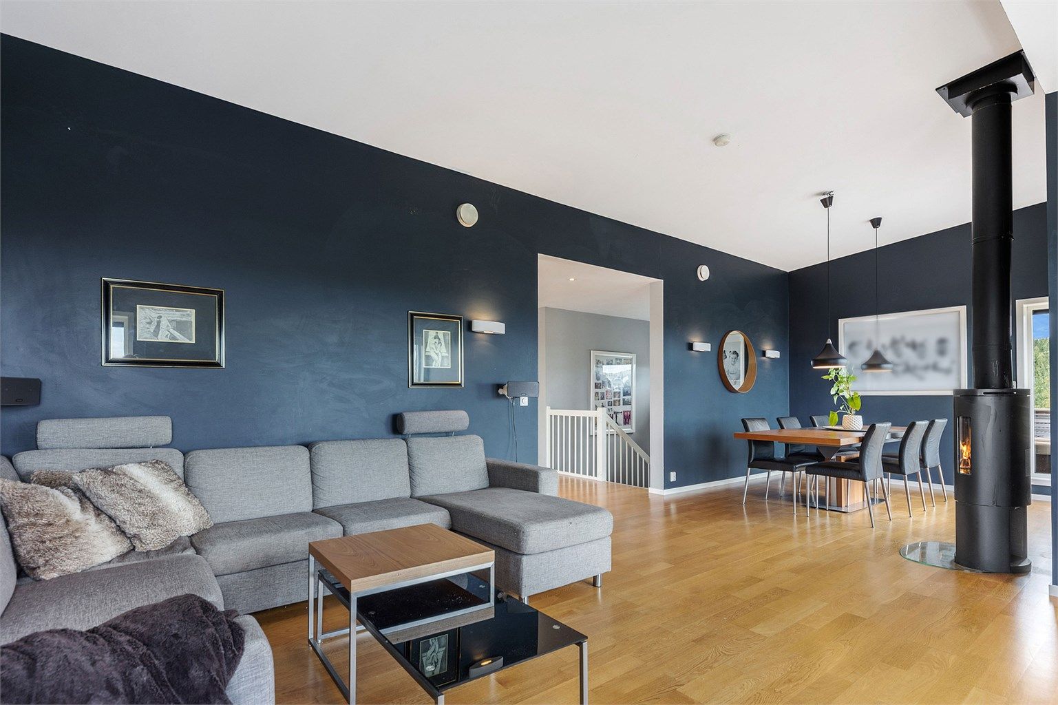 Rommet har god plass til både sofagruppe og spisebord. Peisovnen er strategisk plassert midt mellom.