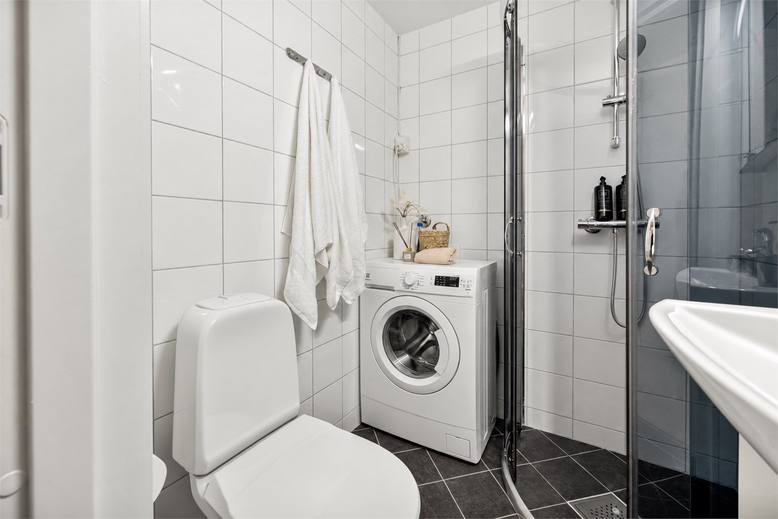 Badet har vegghengt servantinnredning med ovenpåliggende servant, armatur og speil med overlys og stikkontakt. Dusjhjørne med innfellbare dører, vegghengt dusjarmatur og gulvstående toalett.