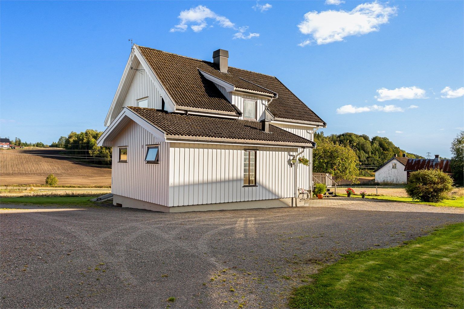 Våningshuset har stående kledning og tak tekket med betongtakstein.