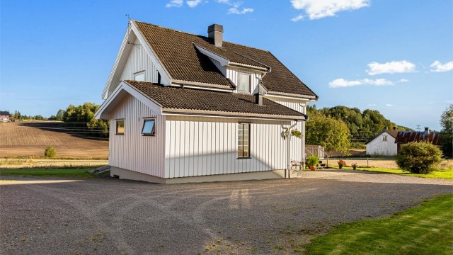 Våningshuset har stående kledning og tak tekket med betongtakstein.
