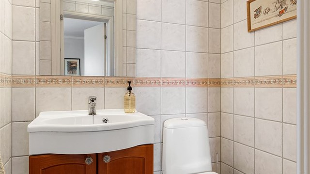 Toalettrom med gulvflate belagt med fliser og gulvvarme. Flislagte vegger. Malte flater i himling. Vegghengt servantinnredning. Ovenpåliggende servant med armatur. Gulvstående toalett.