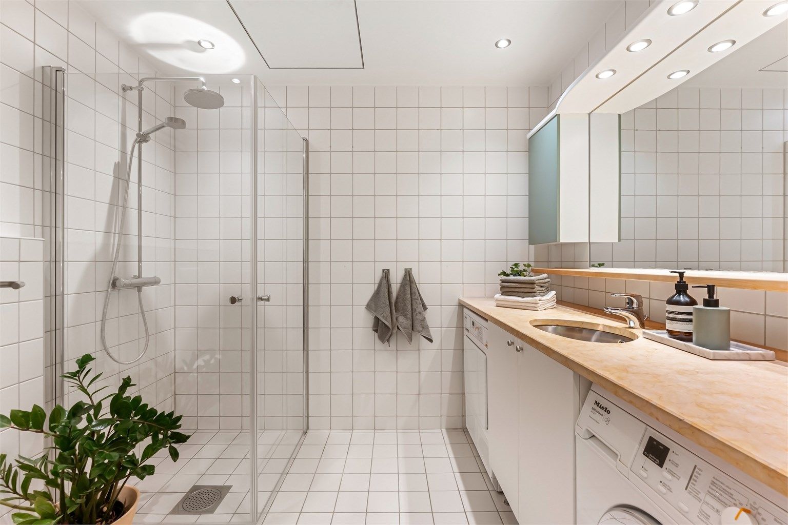 Flislagt baderom med gulvvarme, downlights, regndusj og opplegg for vaskemaskin.