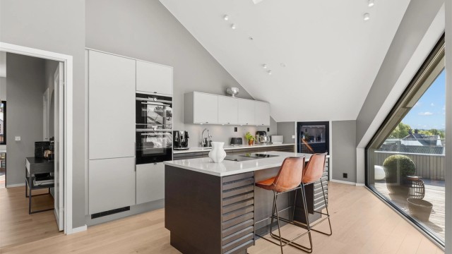 Kjøkkenet fra Sigdal fremstår som både elegant og funksjonelt, med mørke, profilerte lamellfronter og benkeplater i stein. Her er det lagt stor vekt på kvalitet og design, med gode arbeidsflater og en løsning som inviterer til sosial matlaging.