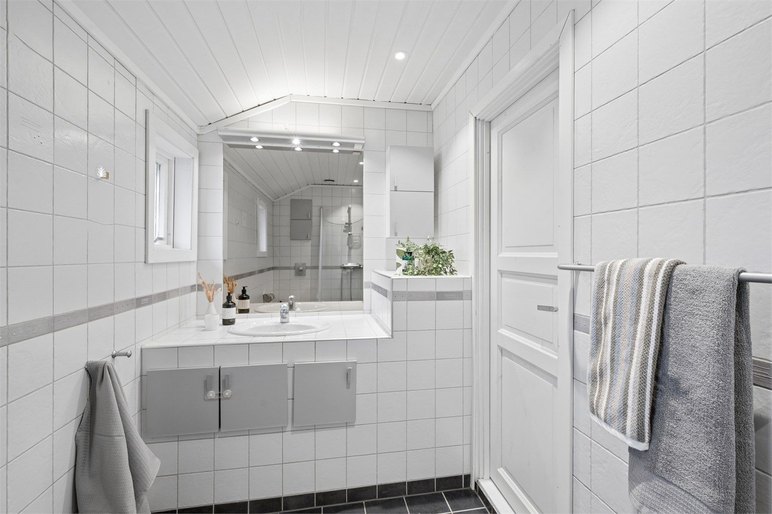 Lyst og pent flislagt bad med gulvvarme, downlights og plassbygd servantinnredning.