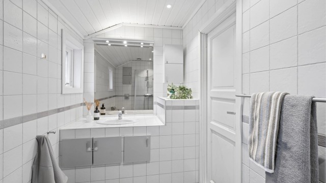 Lyst og pent flislagt bad med gulvvarme, downlights og plassbygd servantinnredning.