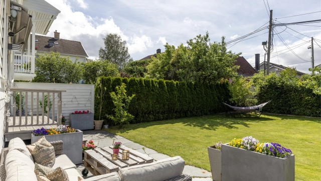 Det er montert markise over trappen ned til hagen. Sommerbilder tatt i 2025 for å illustrere hvordan eiendommen ser ut på sommeren.
