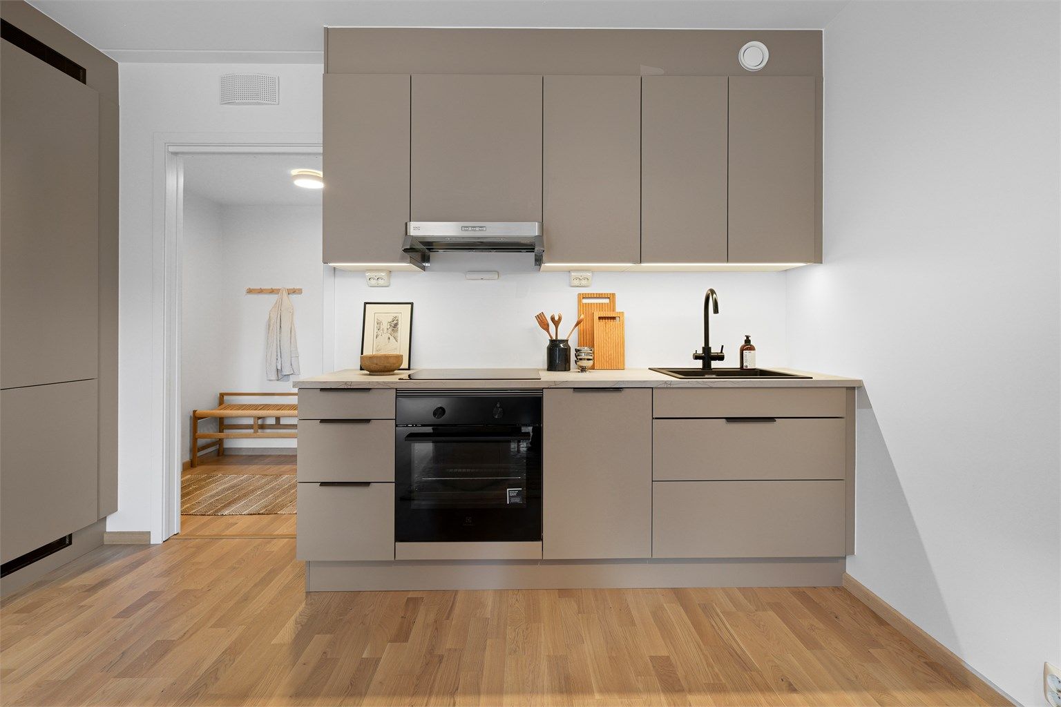 Moderne kjøkken fra HTH med glatte fronter og benkeplate av laminat. Det er nedfelt kjøkkenvask med armatur, benkeskapsbelysning og stikkontakter over kjøkkenbenk.