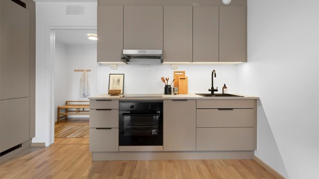 Moderne kjøkken fra HTH med glatte fronter og benkeplate av laminat. Det er nedfelt kjøkkenvask med armatur, benkeskapsbelysning og stikkontakter over kjøkkenbenk.
