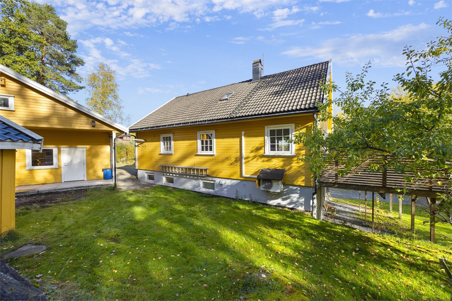 Eiendommen ligger i et lunt terreng med pent opparbeidet plen og frodige trær.