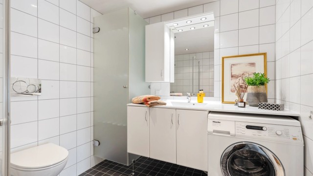 Baderom fra byggeår. Flislagt gulv med gulvvarme. Flislagte vegger. Malte flater i himling. Vegghengt servantinnredning. Ovenpåliggende servant med armatur.
