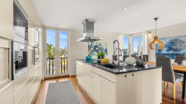 Kjøkkenet har en stilren og funksjonell utforming med plassbygde løsninger, kjøkkenøy og godt med skap- og benkeplass.