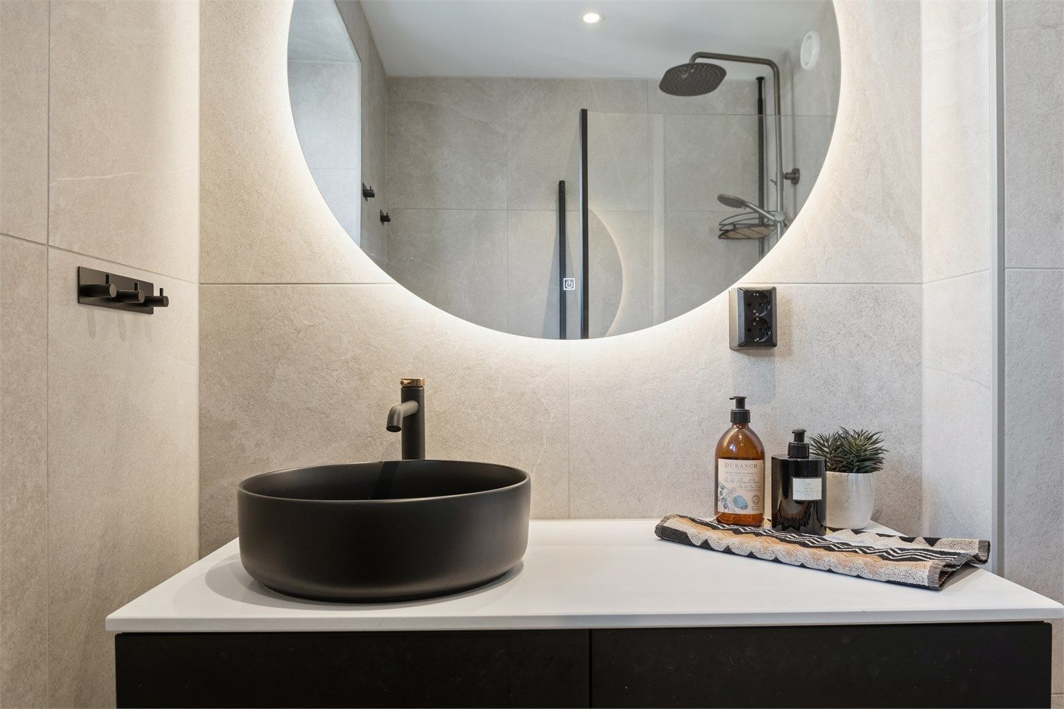 Rommet har flislagte overflater med gulvvarme og er innredet med vegghengt servantinnredning, speil med belysning, dusjhjørne og vegghengt toalett.