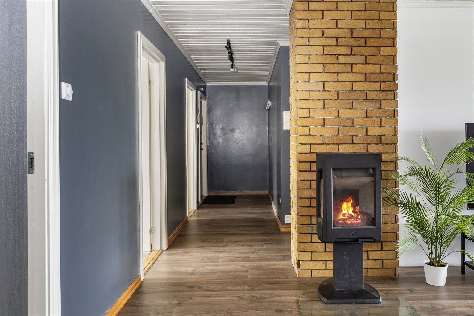 Fra gangen åpner det seg opp mot stuen, hvor peisovnen blir et naturlig midtpunkt.