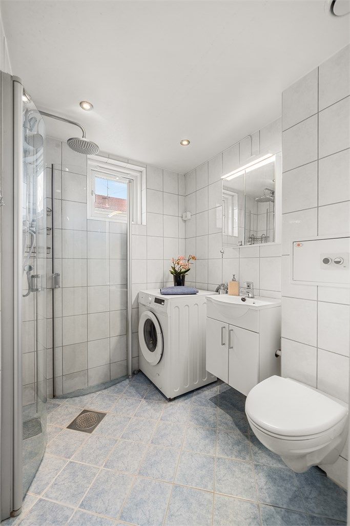 Badet er flislagt og utstyrt med vegghengt toalett, dusjhjørne og downlights i taket.
