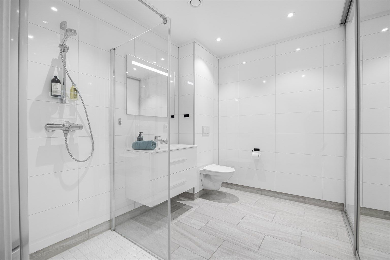 Baderom med vaskerom bak skyvedør med speil.