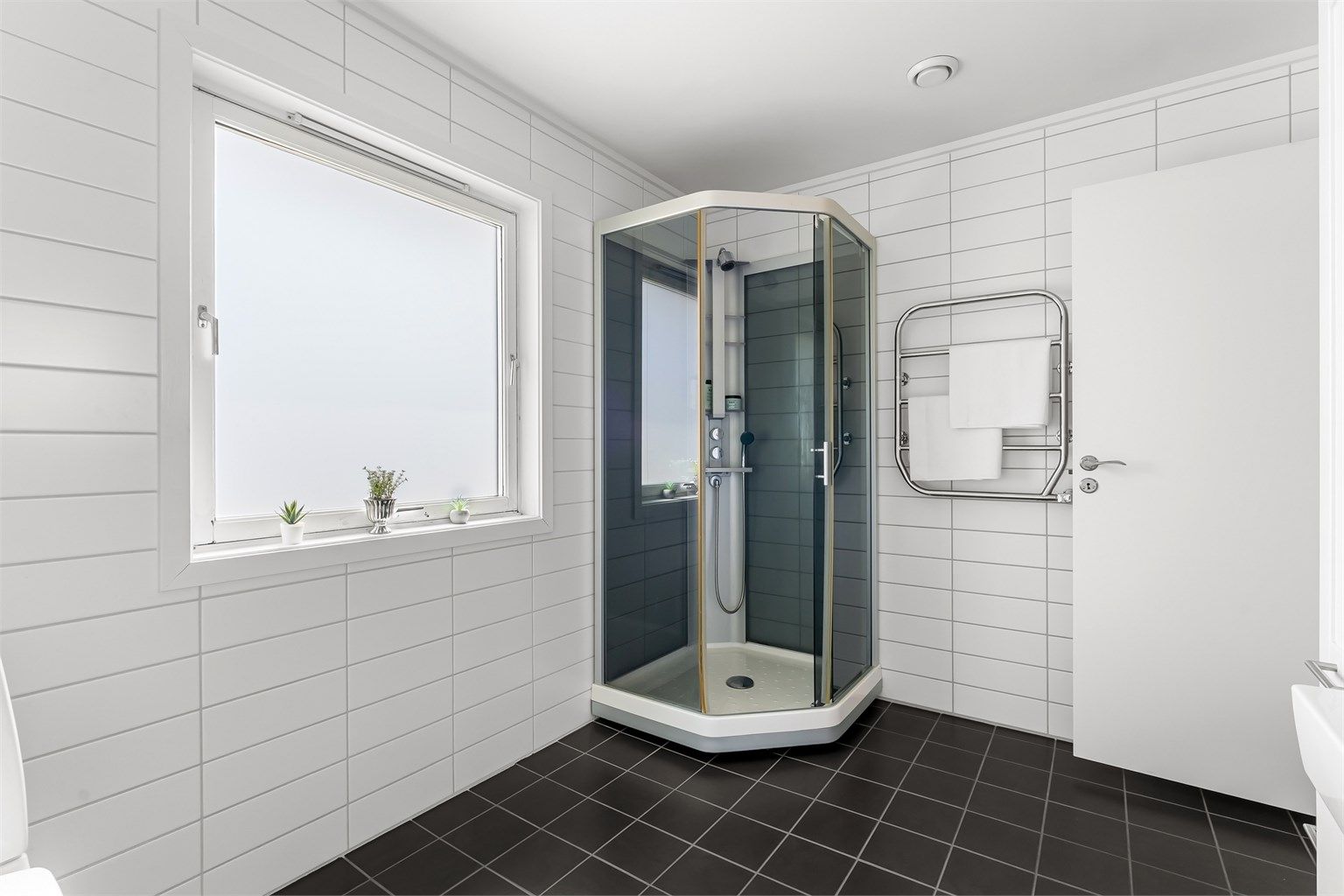 Badet har toalett, vegghengt servantinnredning med ovenpåliggende servant, speilskap med overlys over servant, vegghengt skap og dusjkabinett