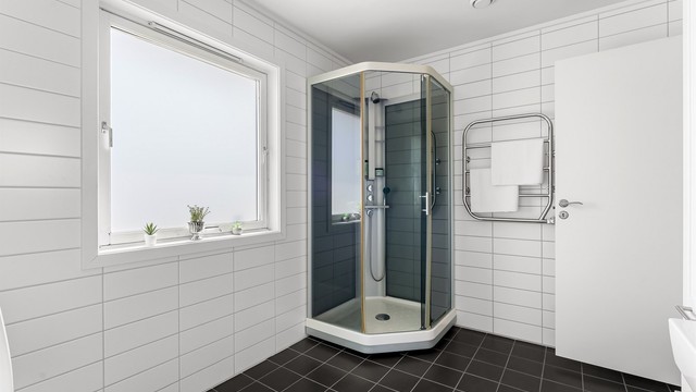 Badet har toalett, vegghengt servantinnredning med ovenpåliggende servant, speilskap med overlys over servant, vegghengt skap og dusjkabinett